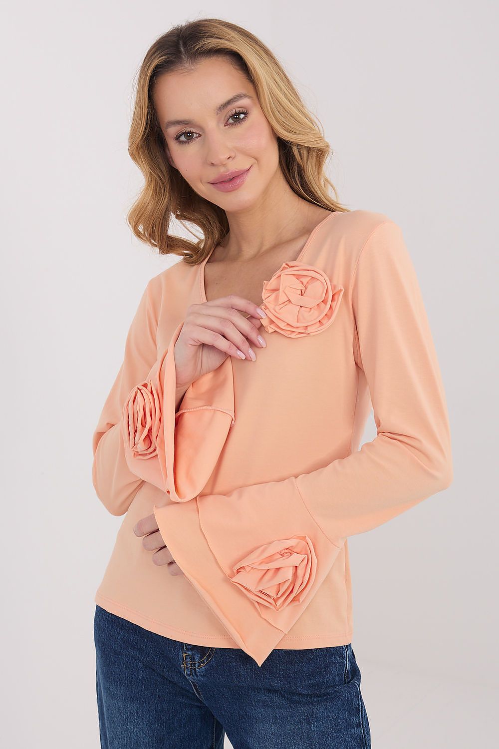 Woman wearing a peach-colored top with floral designs on a plain background