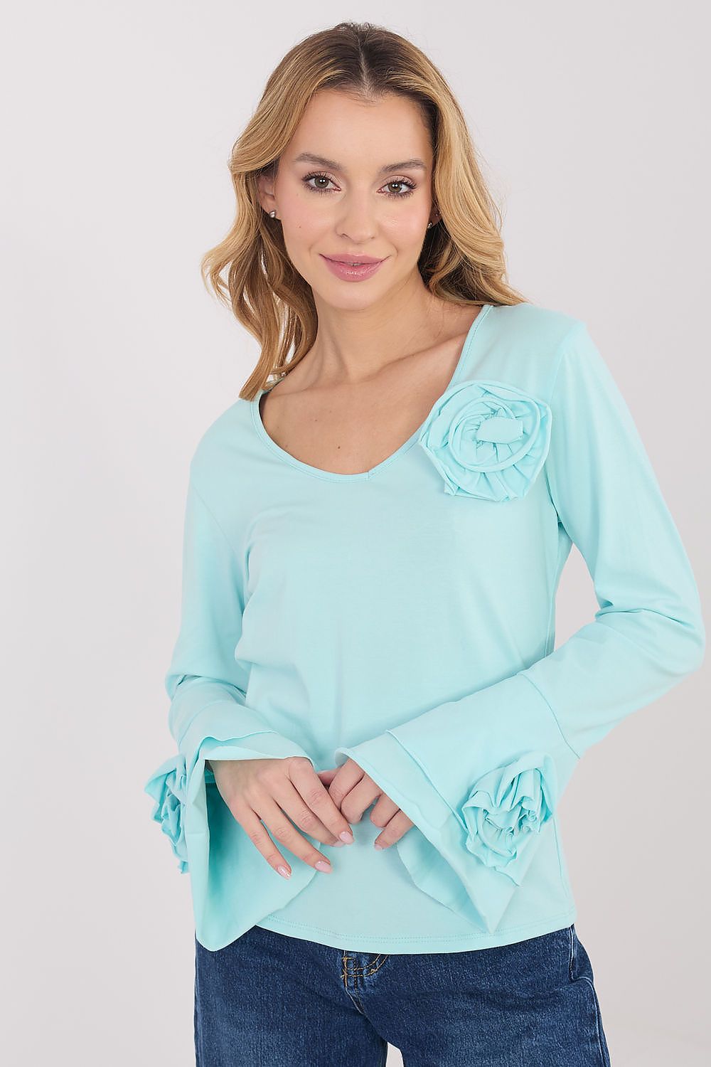 Woman wearing a light blue long-sleeve top with ruffled cuffs on a white background