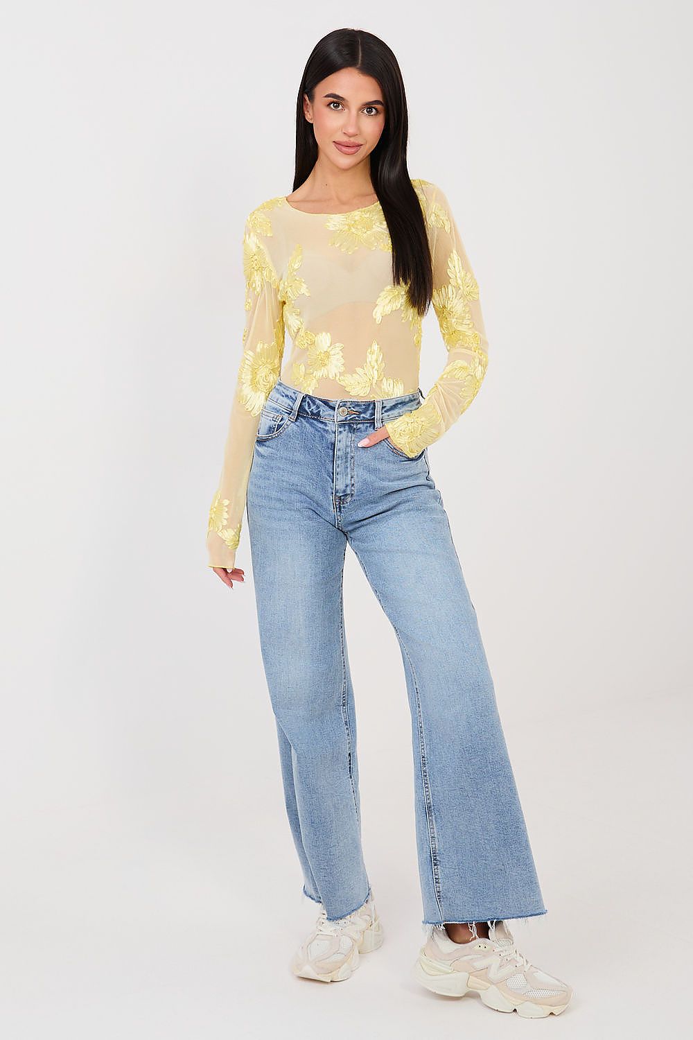 Woman wearing a yellow sequin top and blue jeans on a white background