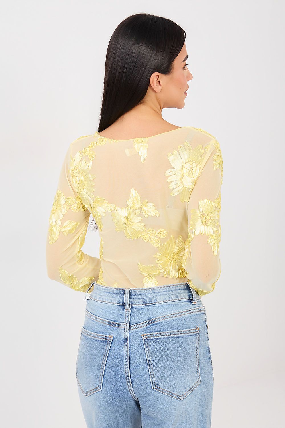 Woman wearing a yellow floral top and blue jeans on a white background