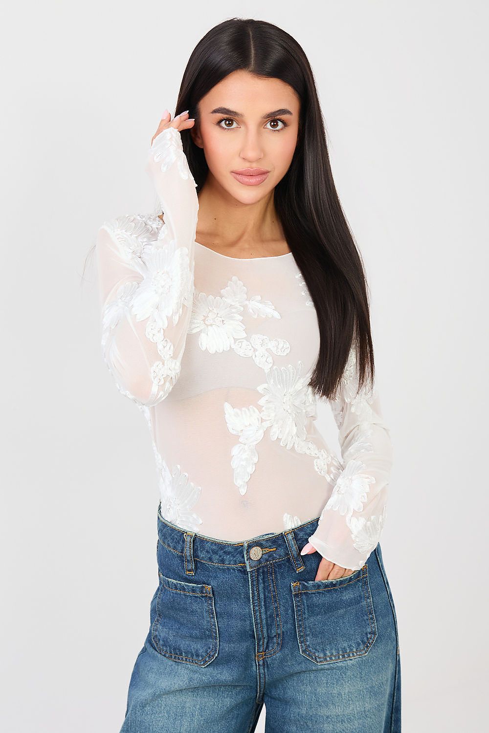 Woman wearing a white floral blouse and blue jeans on a plain background