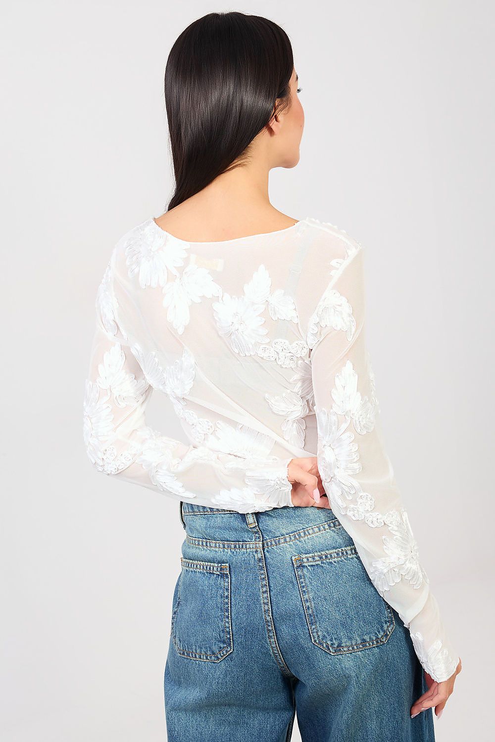 Person wearing a white floral blouse and blue jeans on a plain background