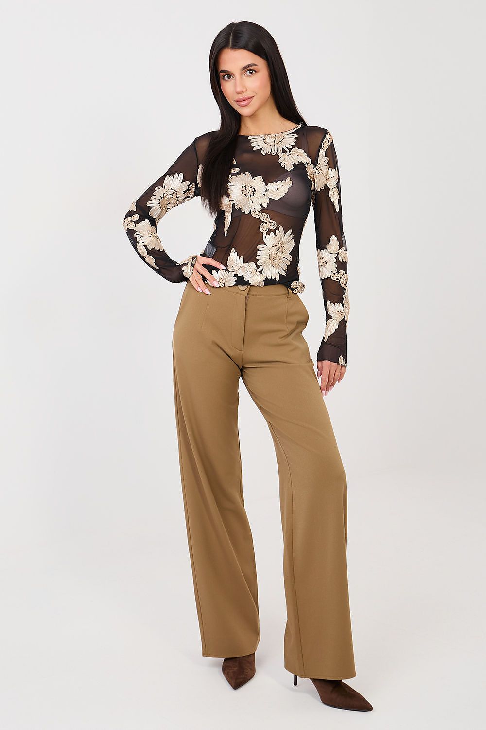 Woman wearing a floral sheer top and beige pants on a white background