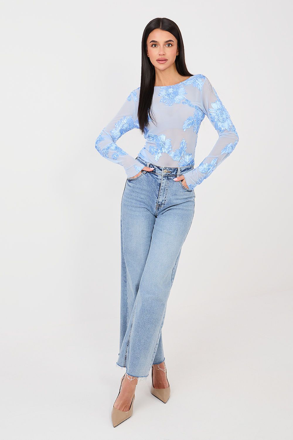 Woman wearing a light blue floral top and jeans on a white background
