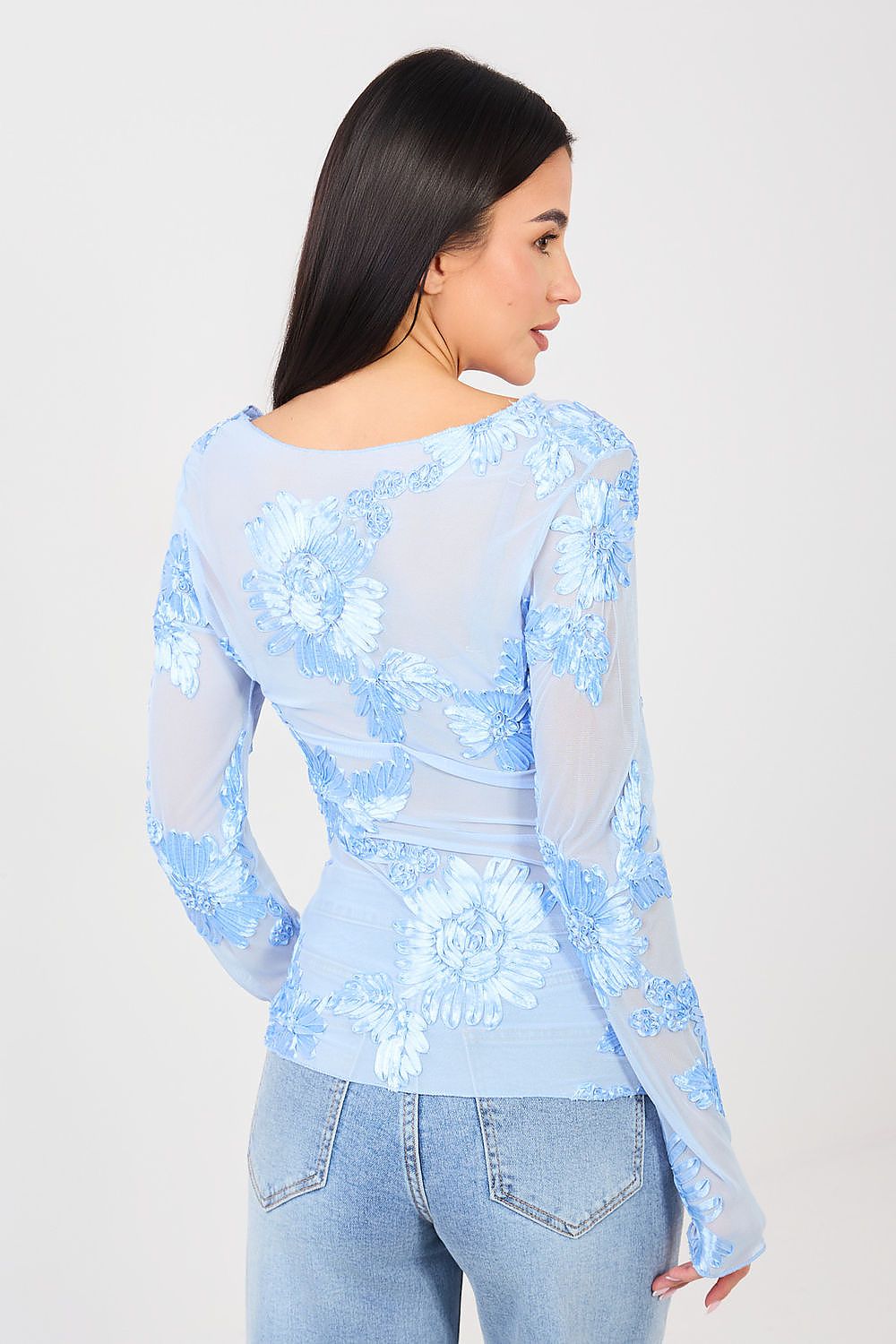 Woman wearing a light blue floral blouse with sheer sleeves on a white background