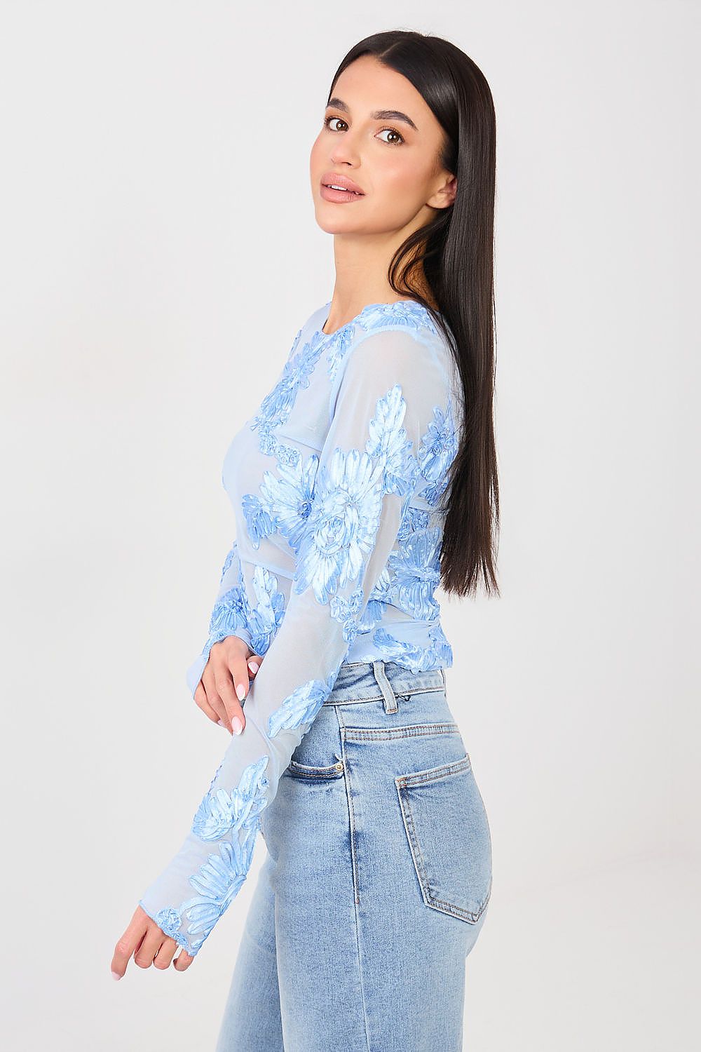Woman wearing a light blue lace top and jeans on a white background