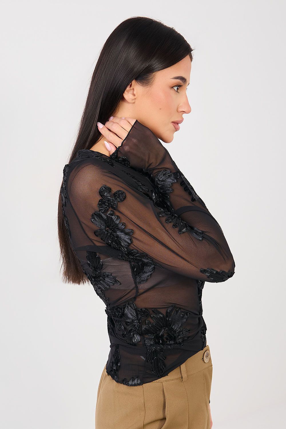 Woman wearing a black sheer top with floral lace details on a white background