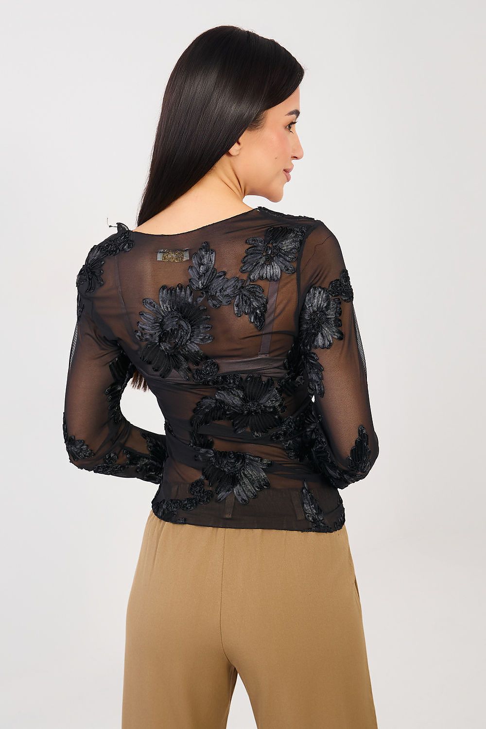 Woman wearing a black floral lace top and beige pants on a white background