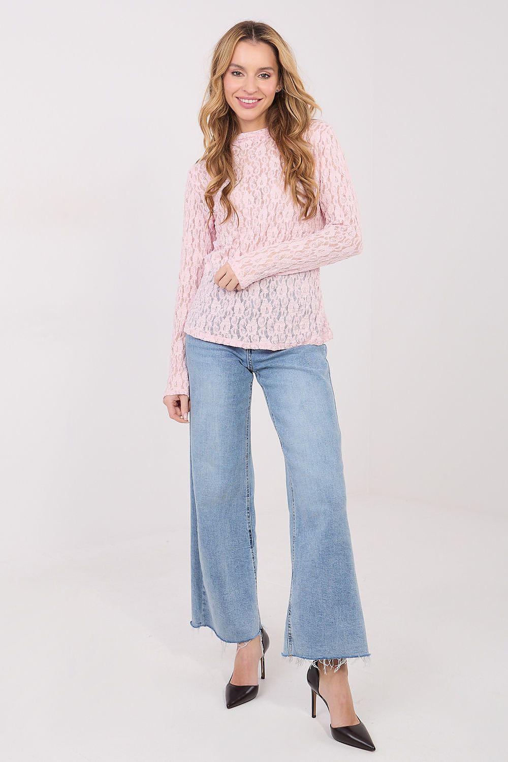Woman wearing a pink lace top and light blue jeans on a white background