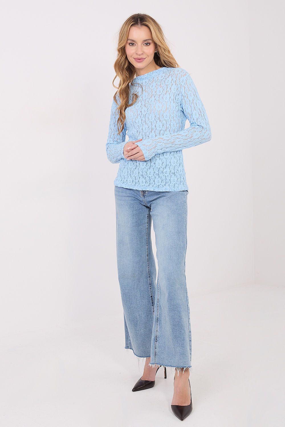 Woman wearing a light blue textured sweater and jeans on a white background
