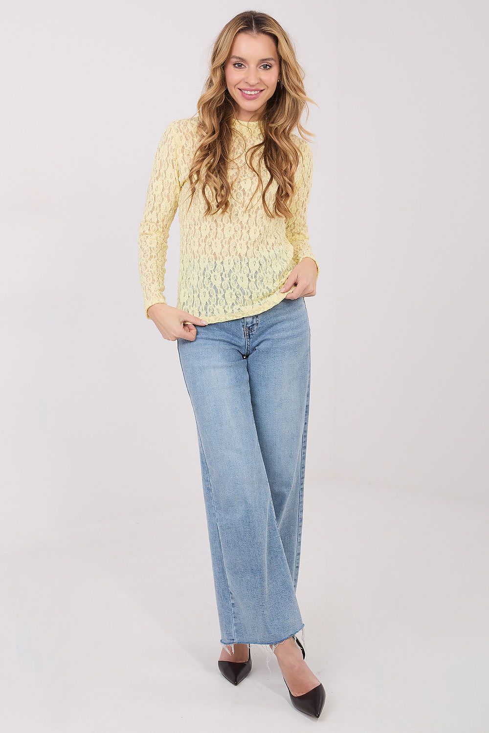 Woman wearing a yellow lace top and blue jeans on a white background