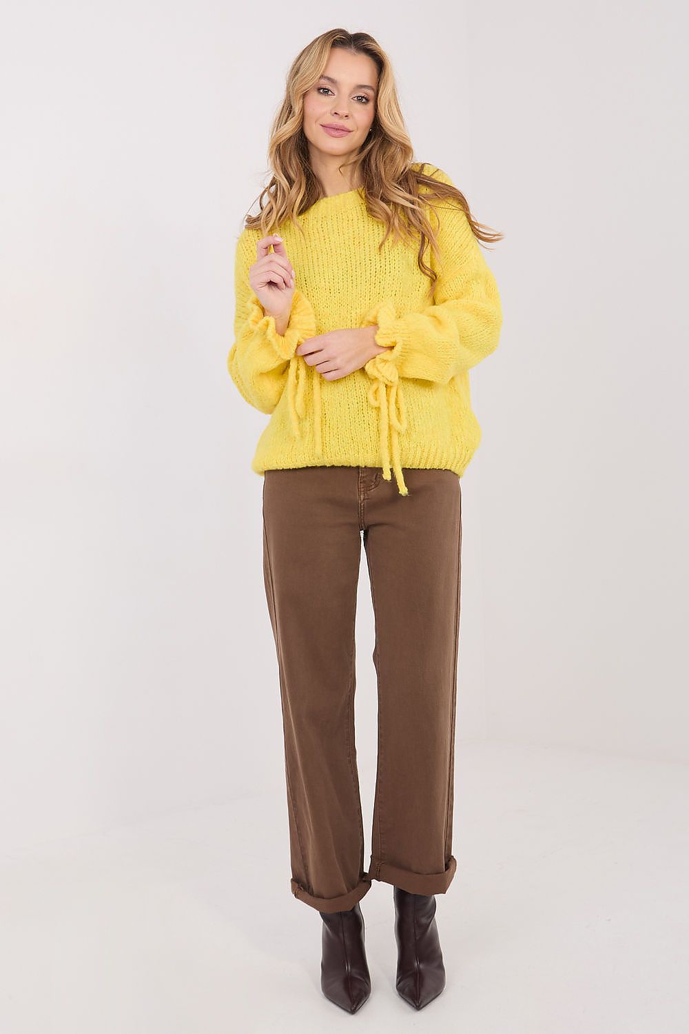 Woman wearing a yellow sweater and brown pants on a white background