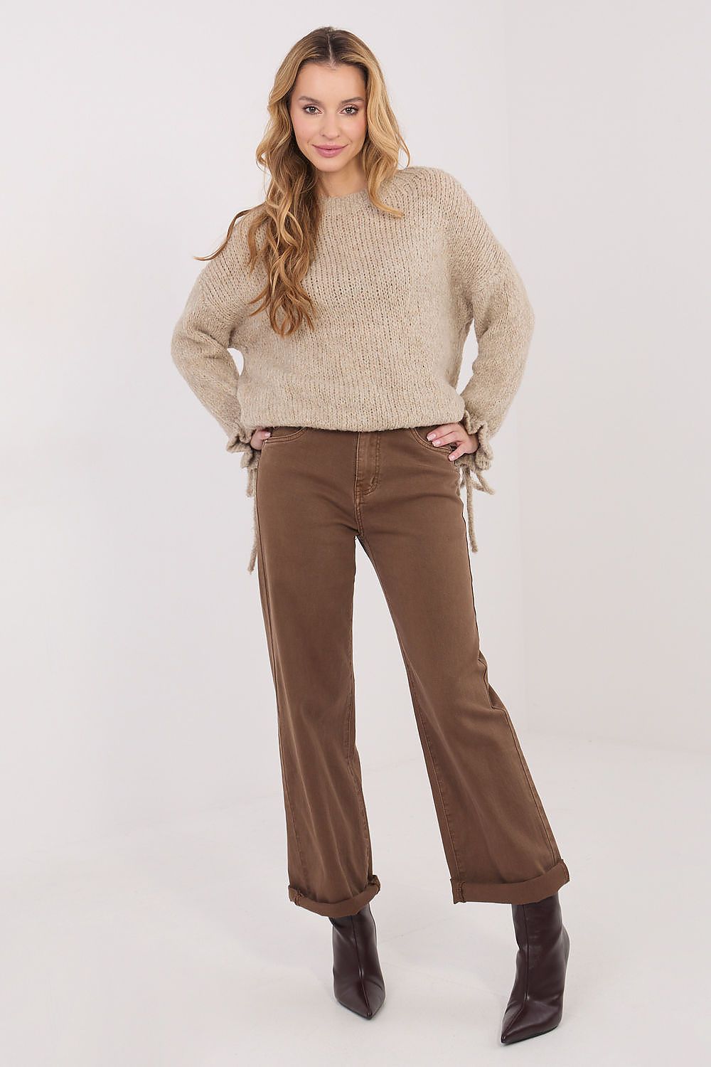 Woman wearing a beige sweater and brown pants on a white background