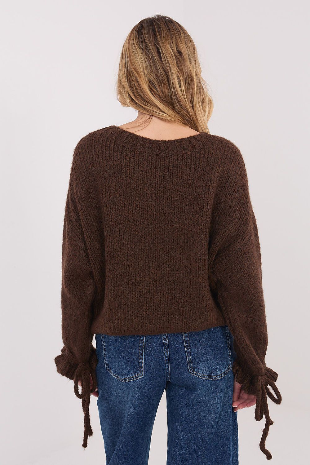 Person wearing a brown sweater and blue jeans on a white background