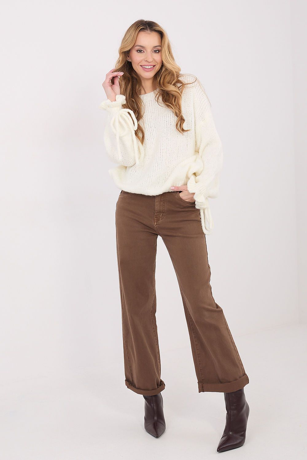 Woman wearing a cream sweater and brown pants on a white background