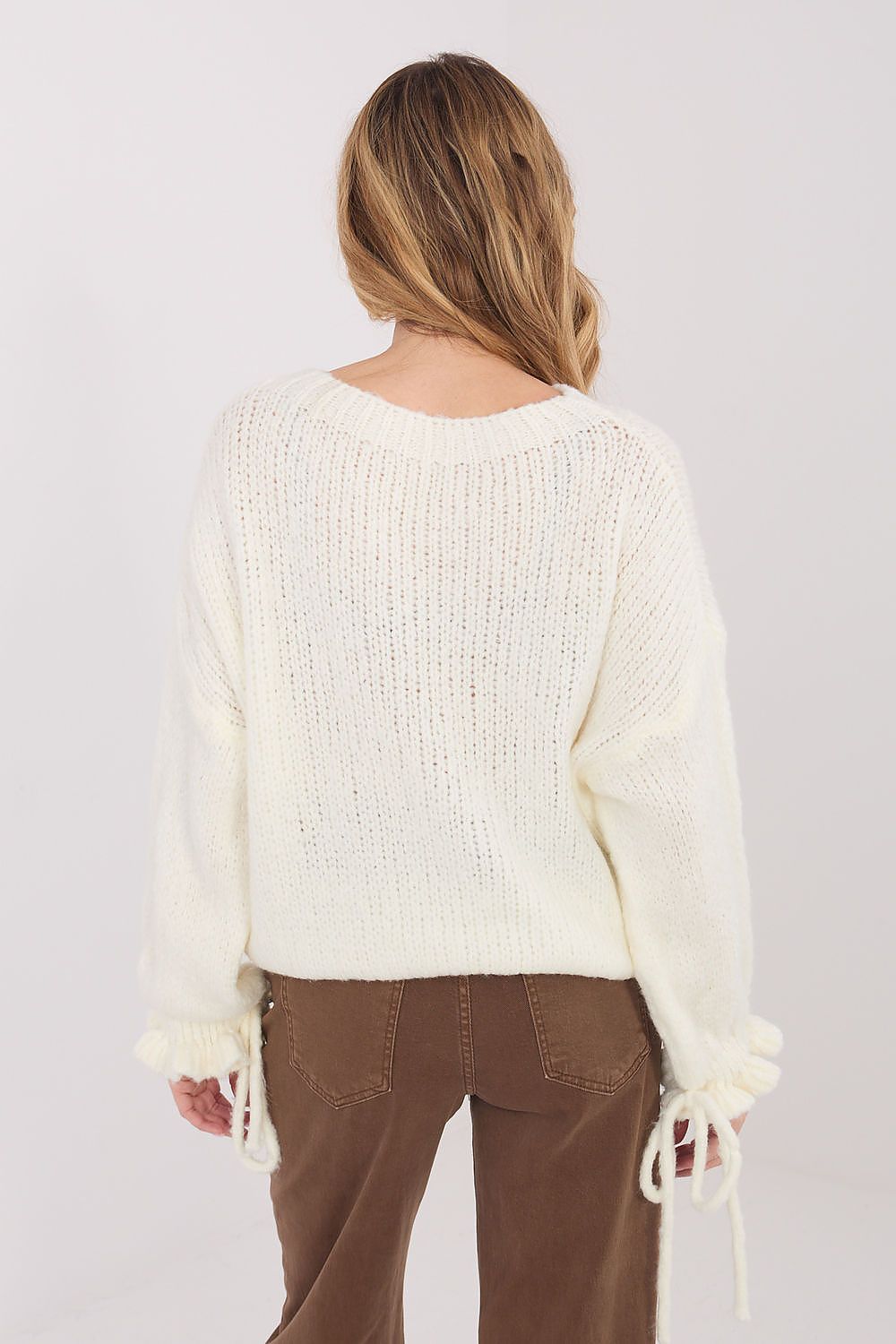 Person wearing a cream sweater and brown pants on a white background