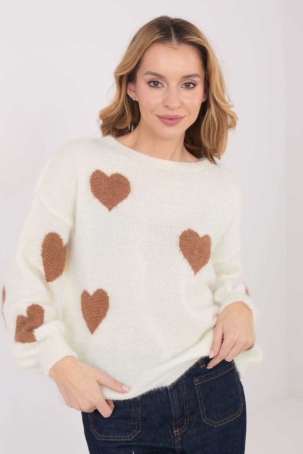 Woman wearing a cream sweater with brown heart patterns on a plain background