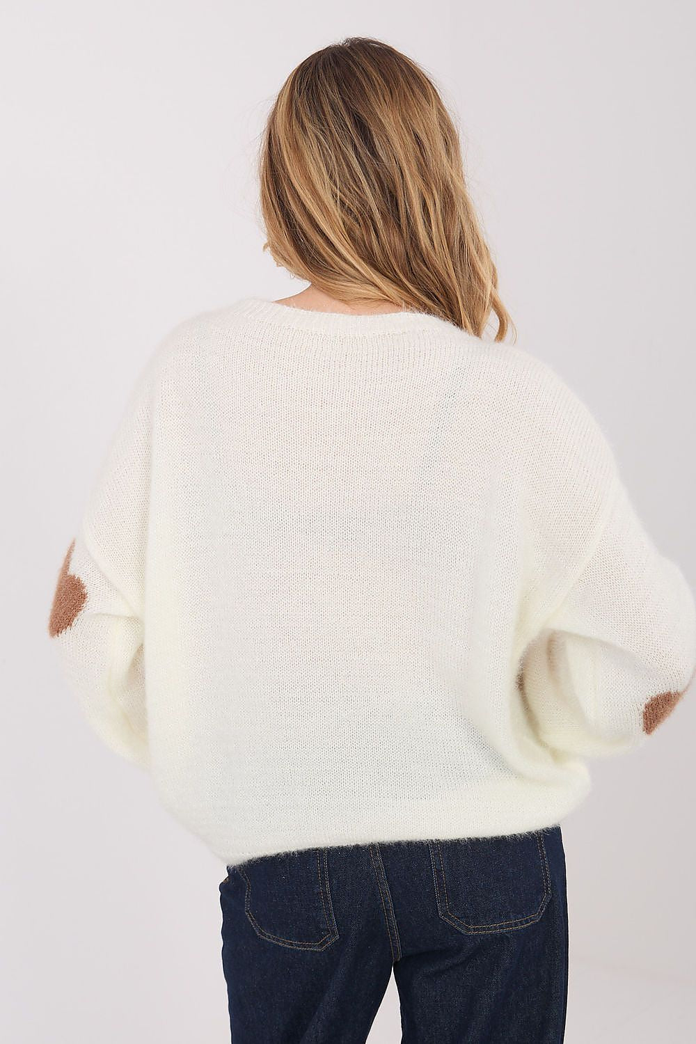 Person wearing a white sweater and dark jeans on a plain background