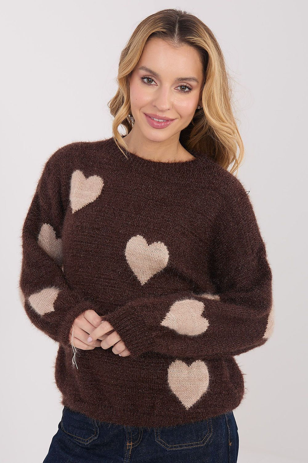 Woman wearing a brown sweater with heart patterns on a plain background