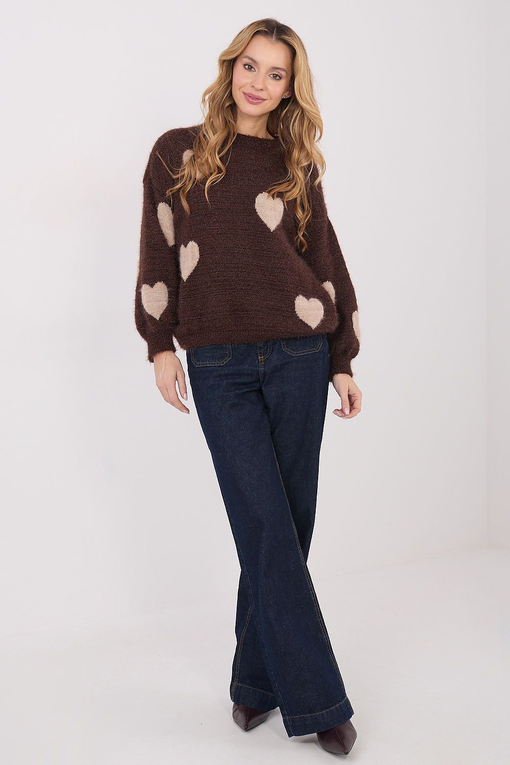 Woman wearing a brown sweater with heart patterns and blue jeans on a white background