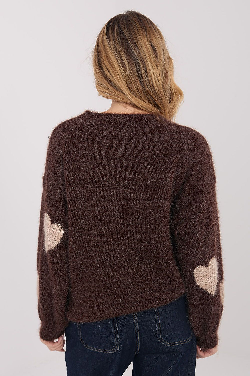 Person wearing a brown sweater with heart patterns on a plain background