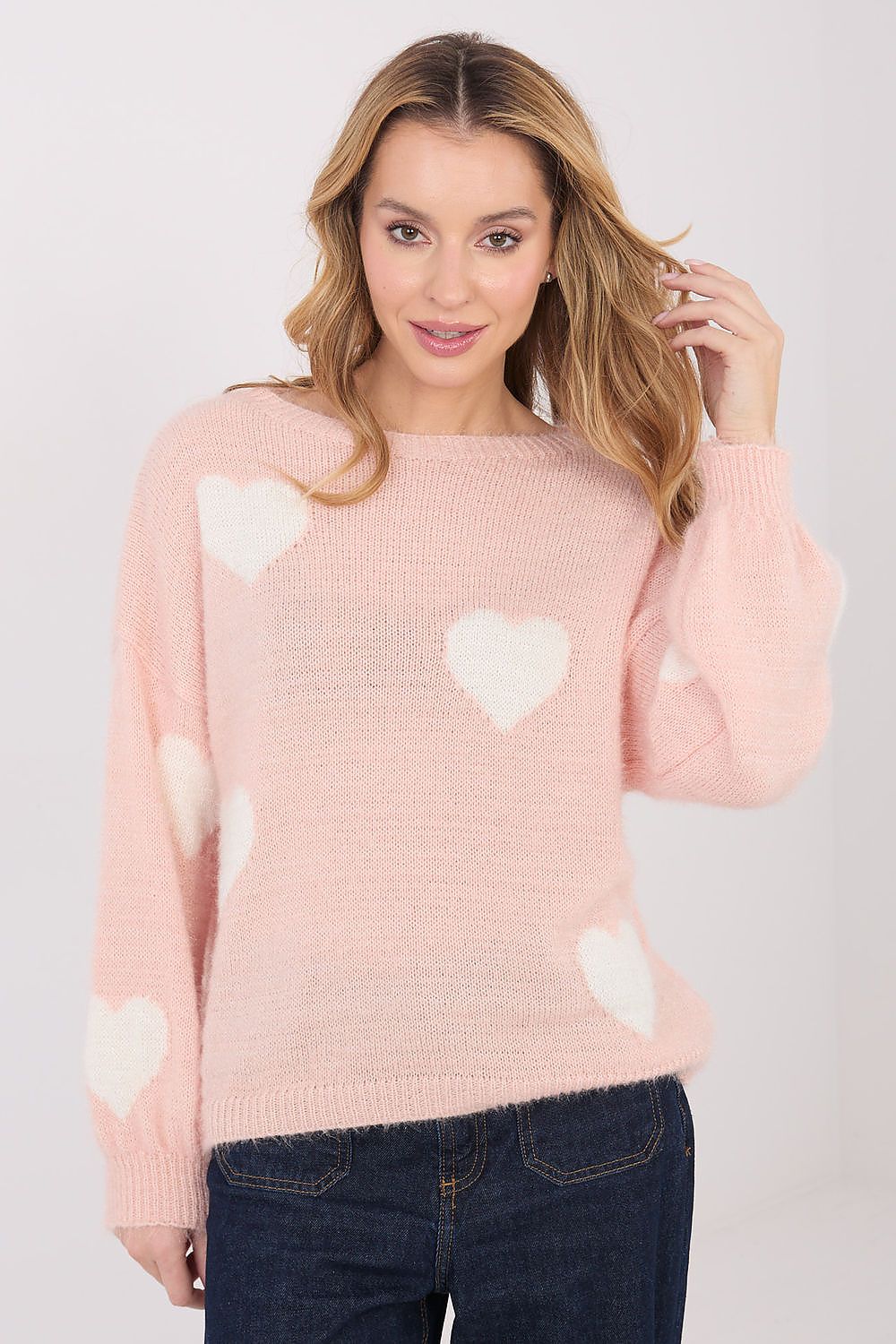 Woman wearing a pink sweater with white heart patterns on a plain background