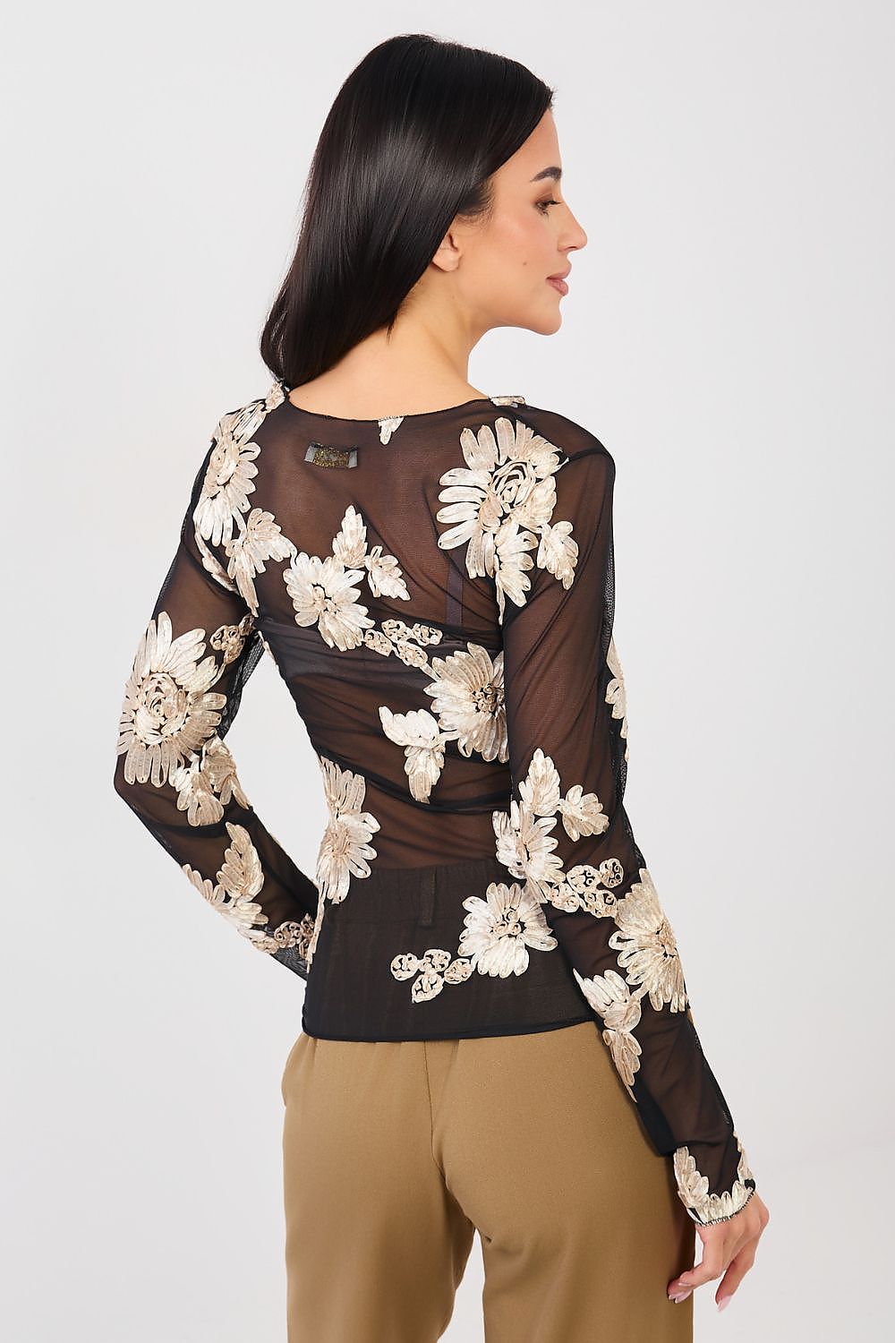 Woman wearing a black long-sleeve top with floral lace details on a white background
