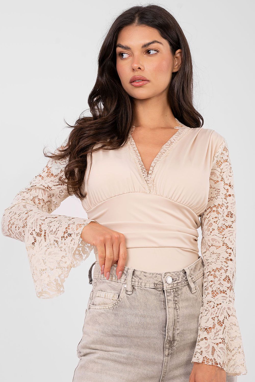 Woman wearing a beige lace top with long sleeves and high-waisted jeans on a white background