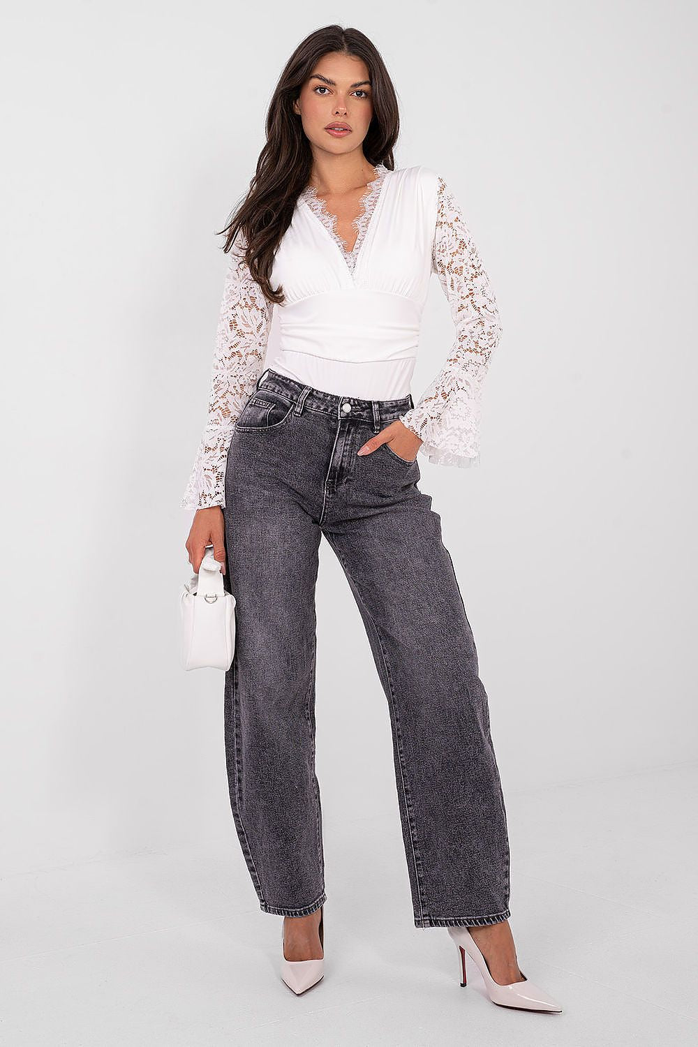 Woman wearing a white blouse with lace sleeves and high-waisted black jeans on a white background