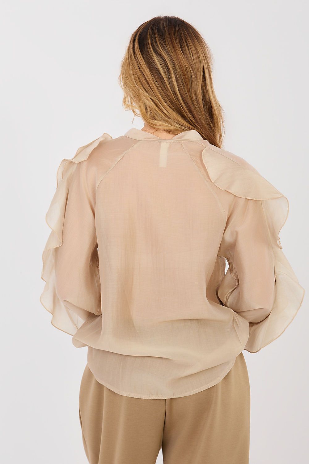 Woman wearing a beige blouse with ruffled sleeves on a white background