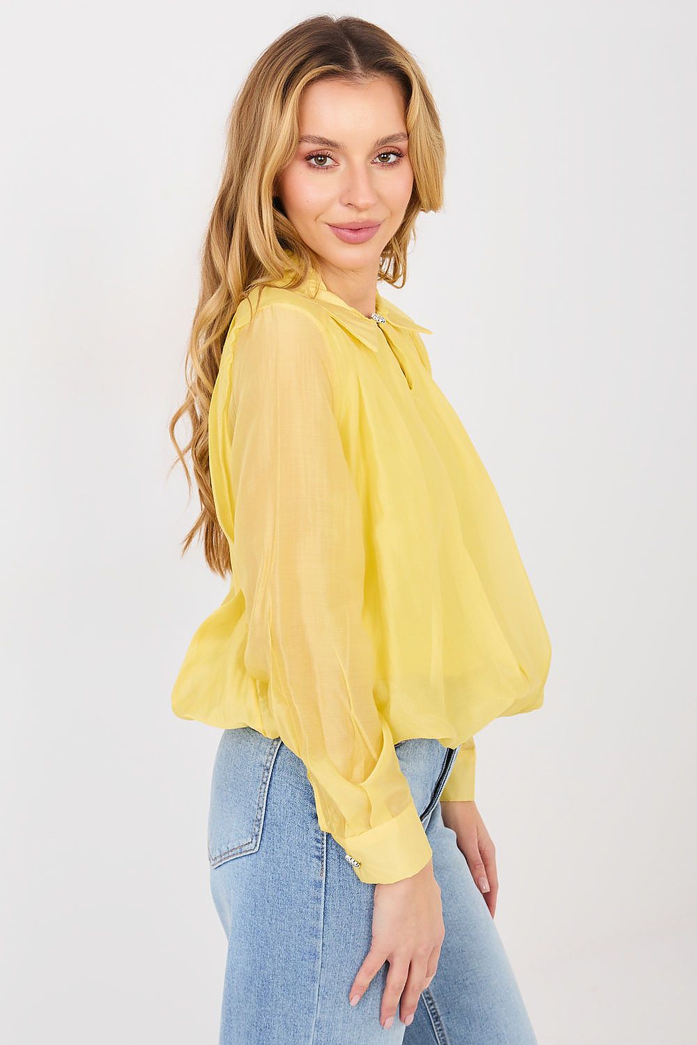 Woman wearing a yellow blouse and blue jeans on a light gray background