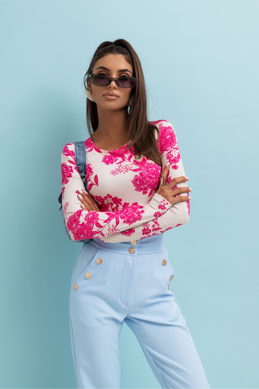 Woman wearing a floral top and light blue pants against a light blue background