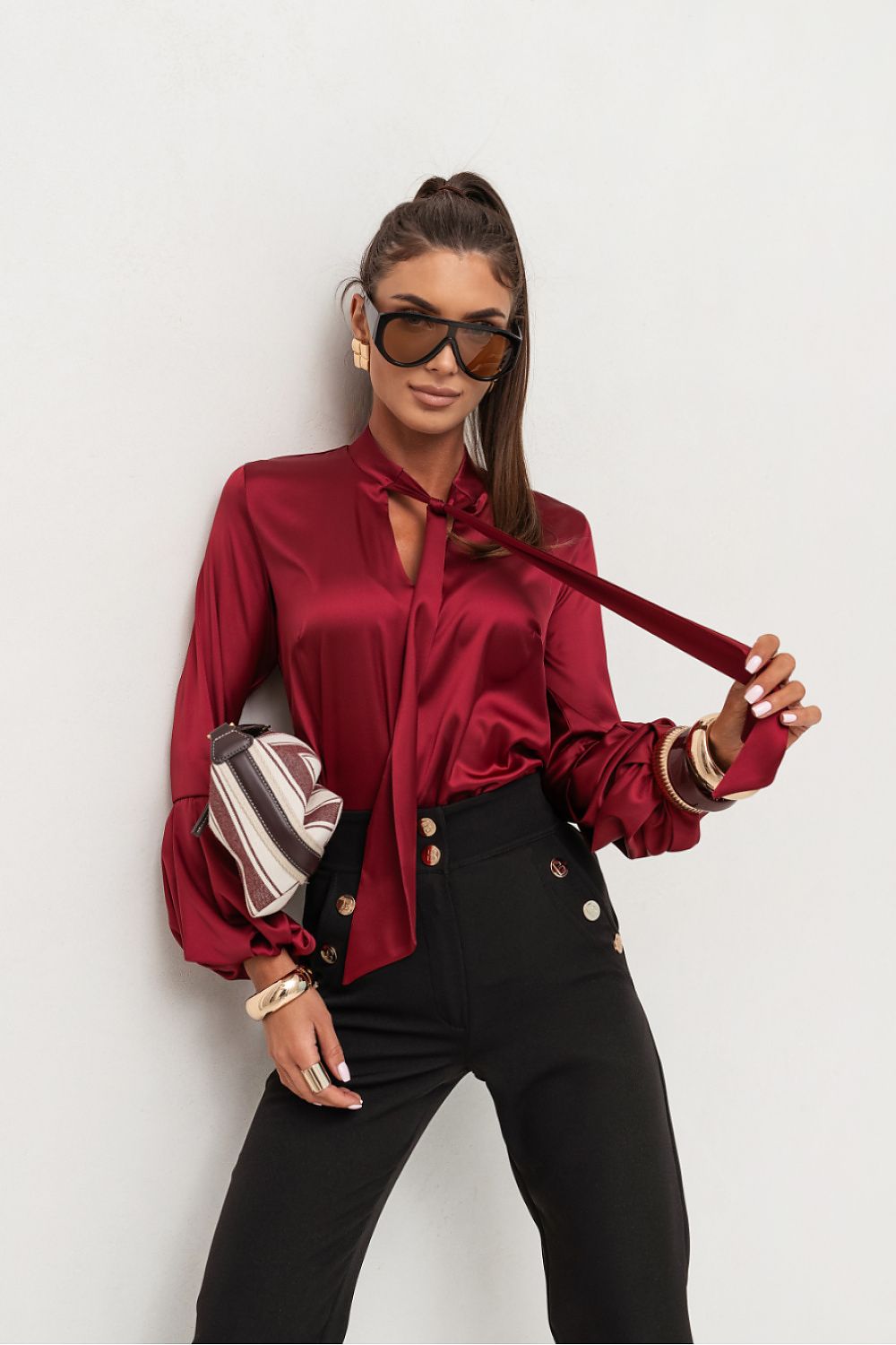 Woman wearing a red blouse with a tie, black pants, and sunglasses on a white background