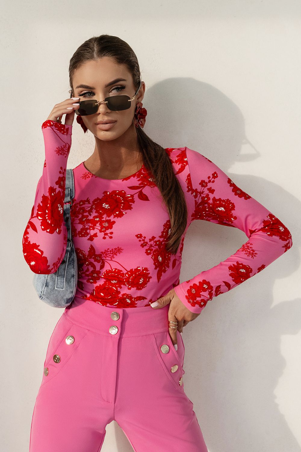 Woman wearing a pink floral top and pants with sunglasses against a white background
