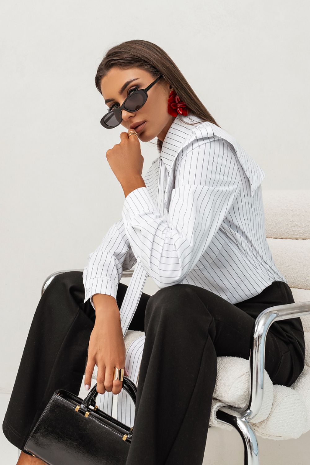 Woman in a white ribbed sweater and black pants sitting on a chair with a white background