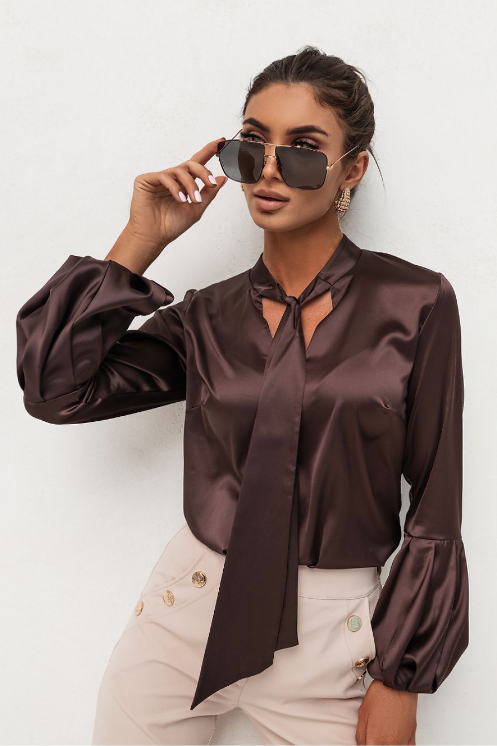 Woman wearing a brown satin blouse and sunglasses against a white background