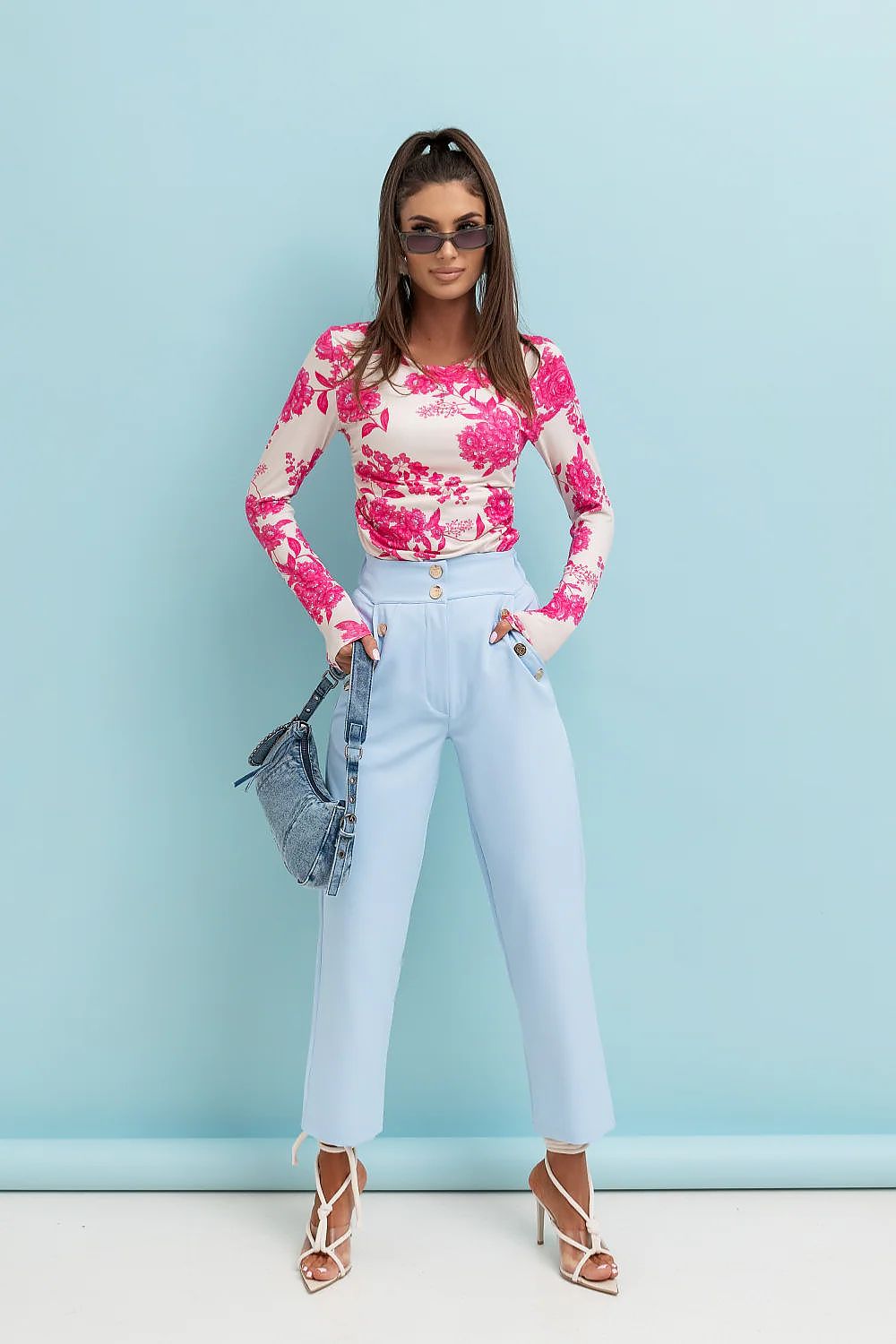 Woman wearing a pink floral top and light blue pants against a light blue background