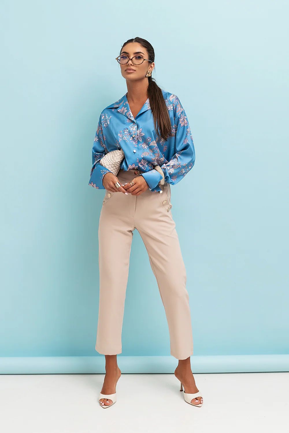 Woman wearing a blue floral blouse and beige pants against a light blue background