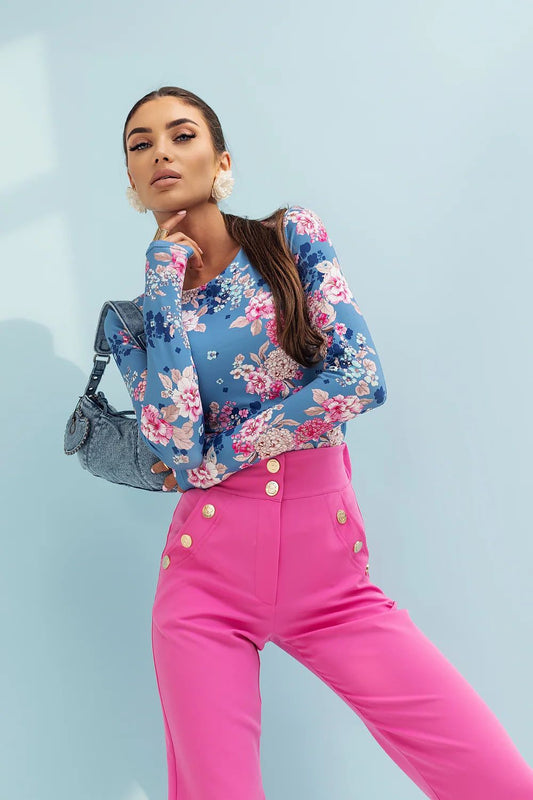 Woman wearing a floral blue top and pink pants with a light blue background