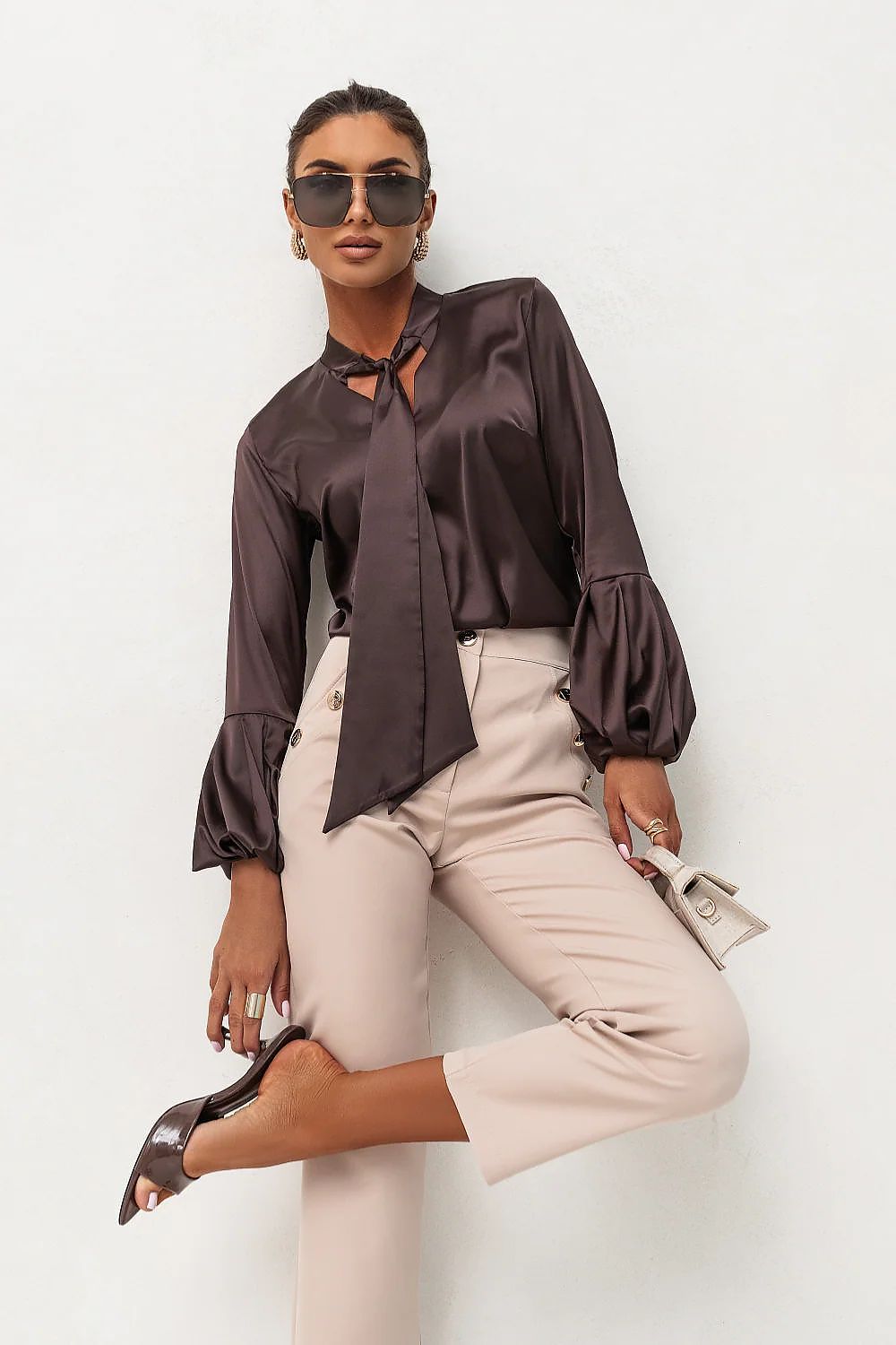 Woman wearing a brown blouse and beige pants against a white background