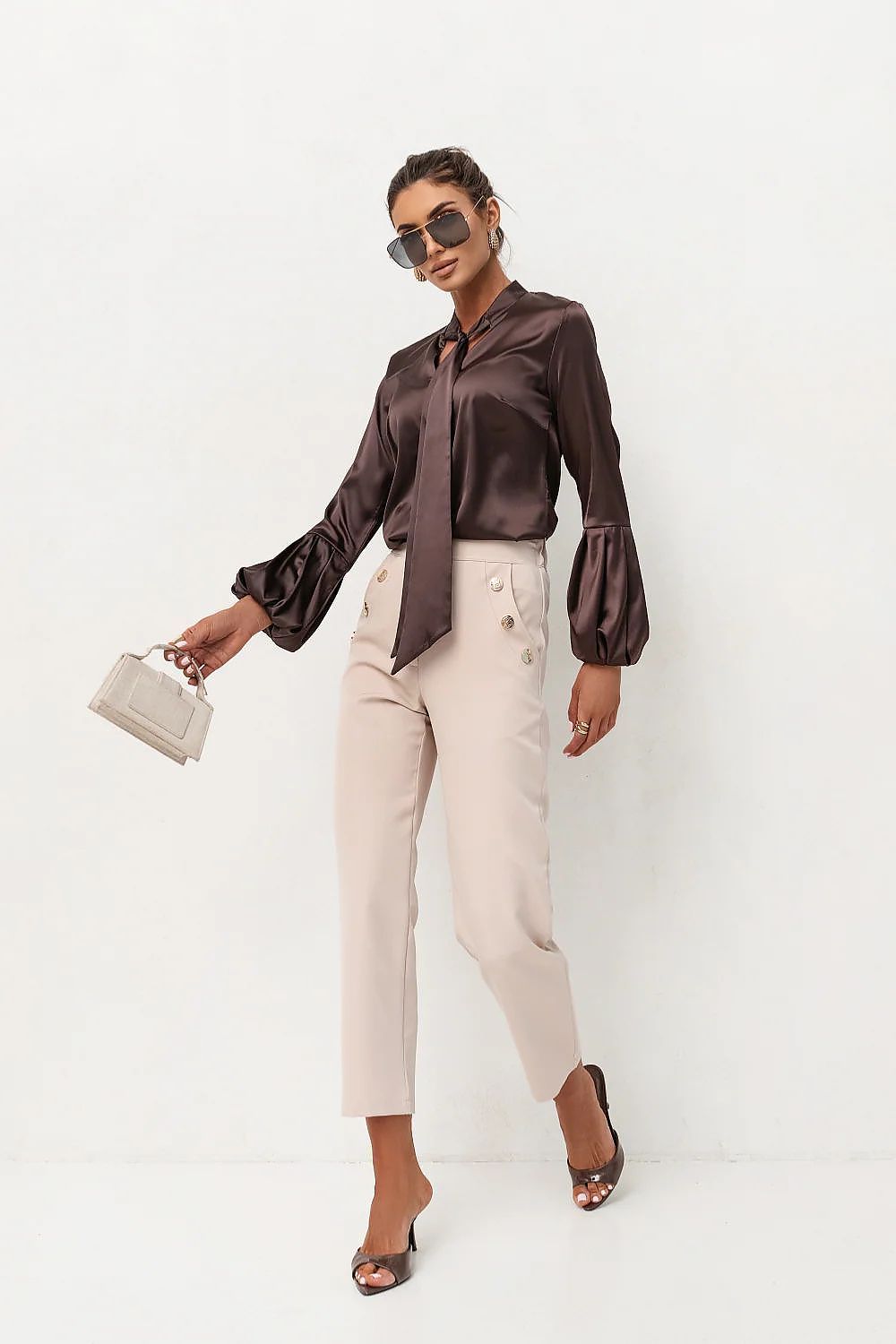 Woman wearing a brown satin blouse and beige pants against a white background