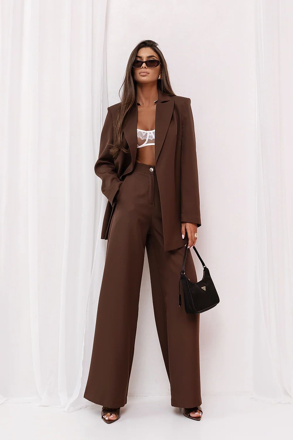 Woman in a brown suit with a white top against a white curtain background