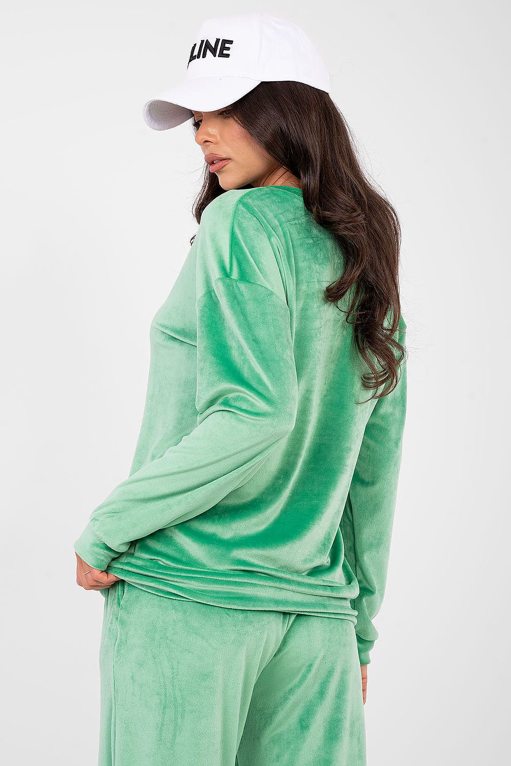 Person wearing a green velour tracksuit and white cap on a white background