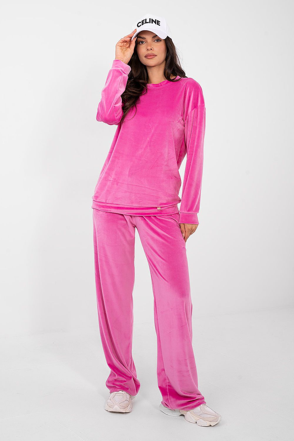 Person wearing a pink velvet outfit with a white Celine hat on a white background