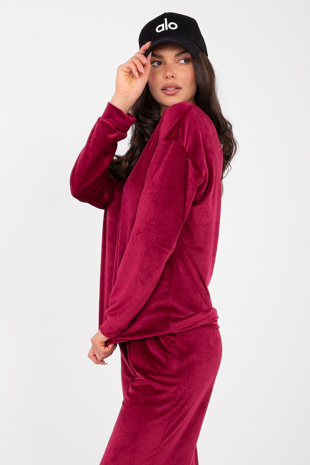Woman wearing a maroon velour tracksuit and black cap with 'alo' logo on a white background