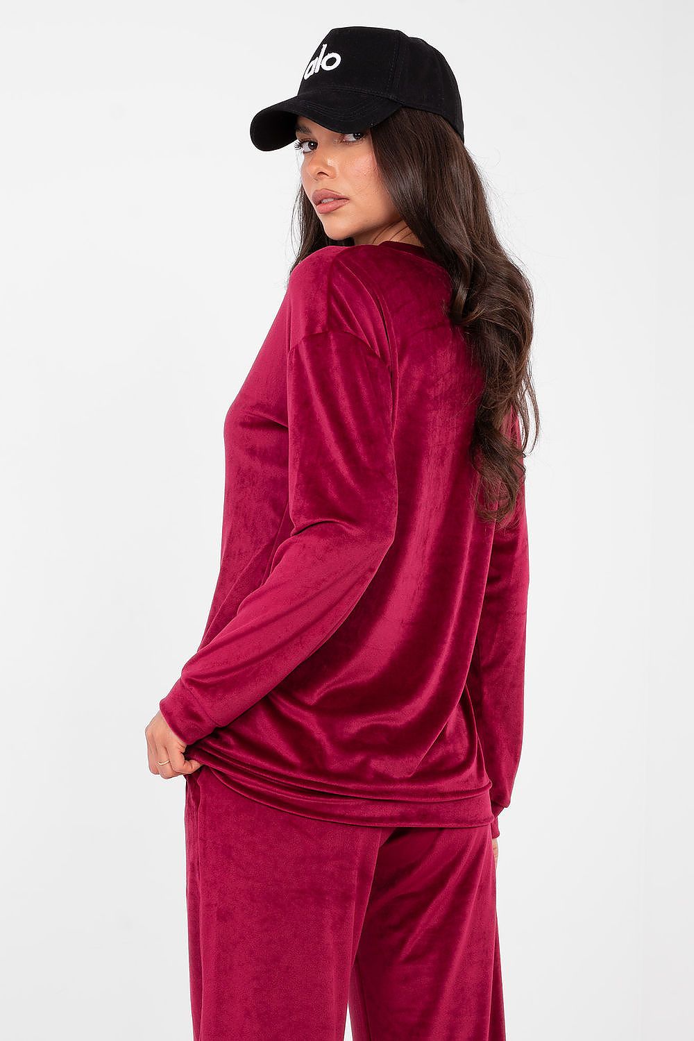 Woman wearing a red velour tracksuit and black cap on a white background