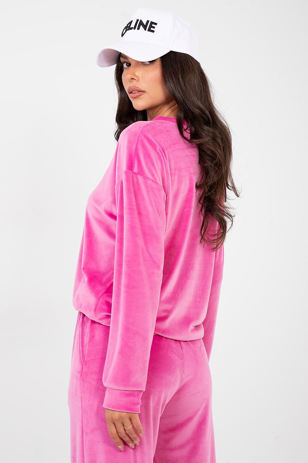 Woman wearing a pink velour tracksuit and white cap with 'INLINE' logo on a white background