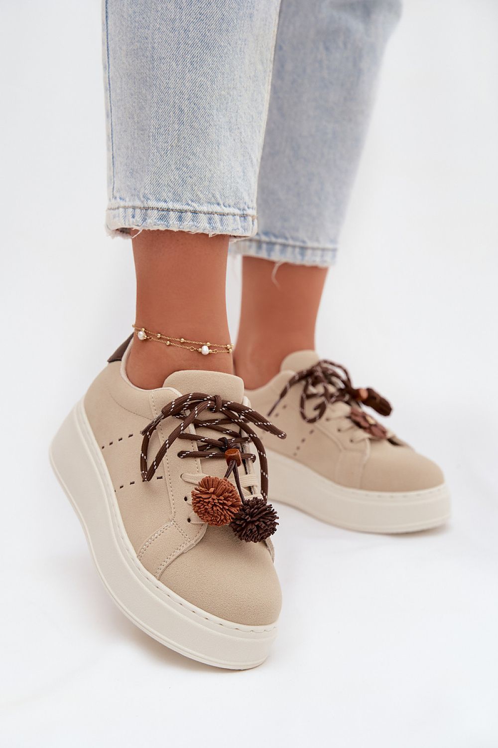 Beige sneakers with brown laces and decorative elements worn with light blue jeans on a white background