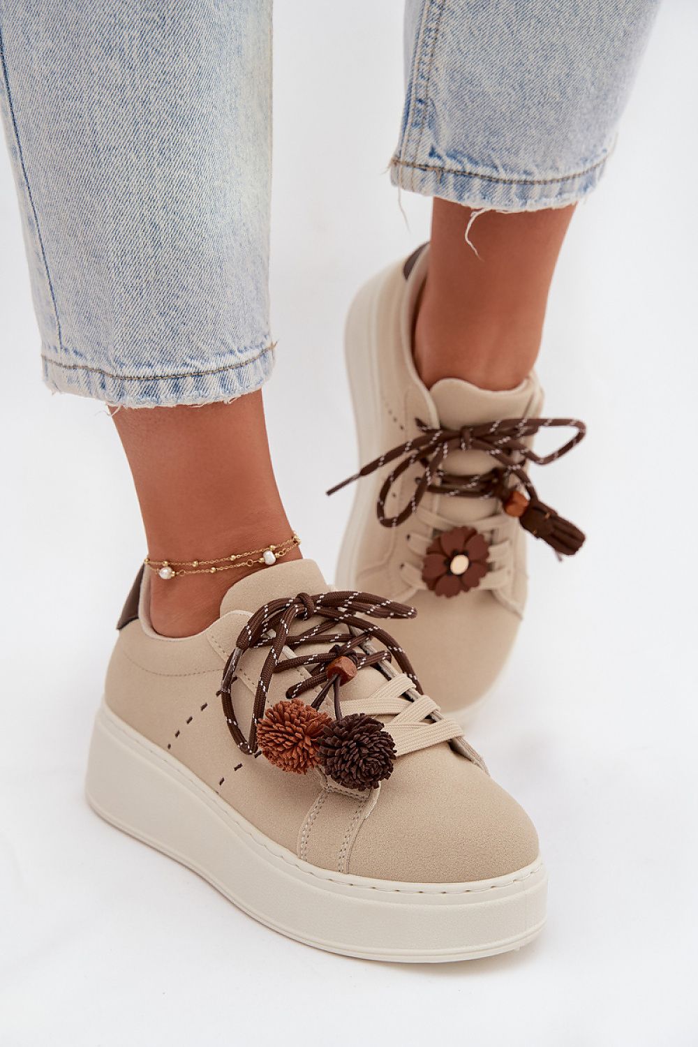 Beige sneakers with brown accents worn with light blue jeans on a white background
