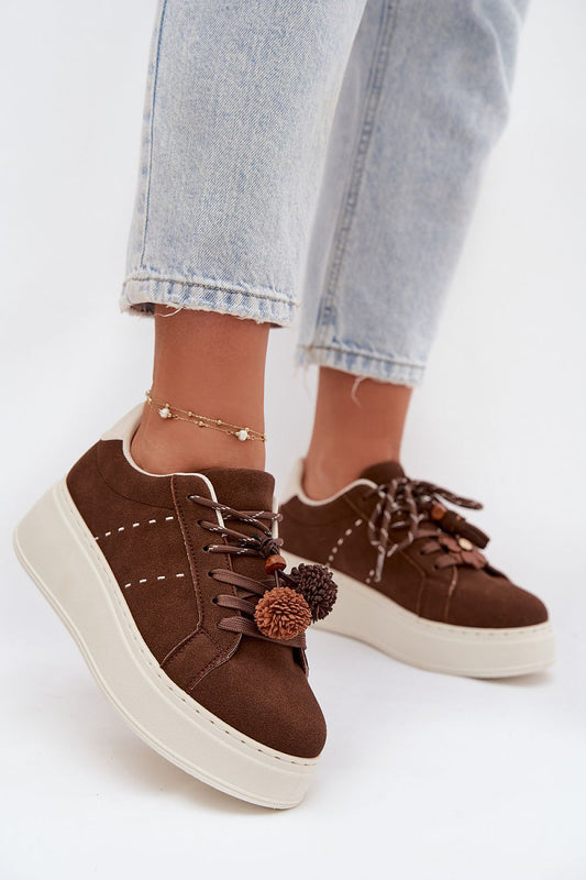 Brown sneakers with pom-poms worn with light blue jeans on a white background